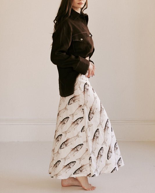 Woman wearing a dark jacket and a long skirt with fish pattern on a plain background