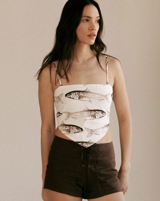 Woman wearing a sleeveless top with fish pattern and brown shorts against a plain background