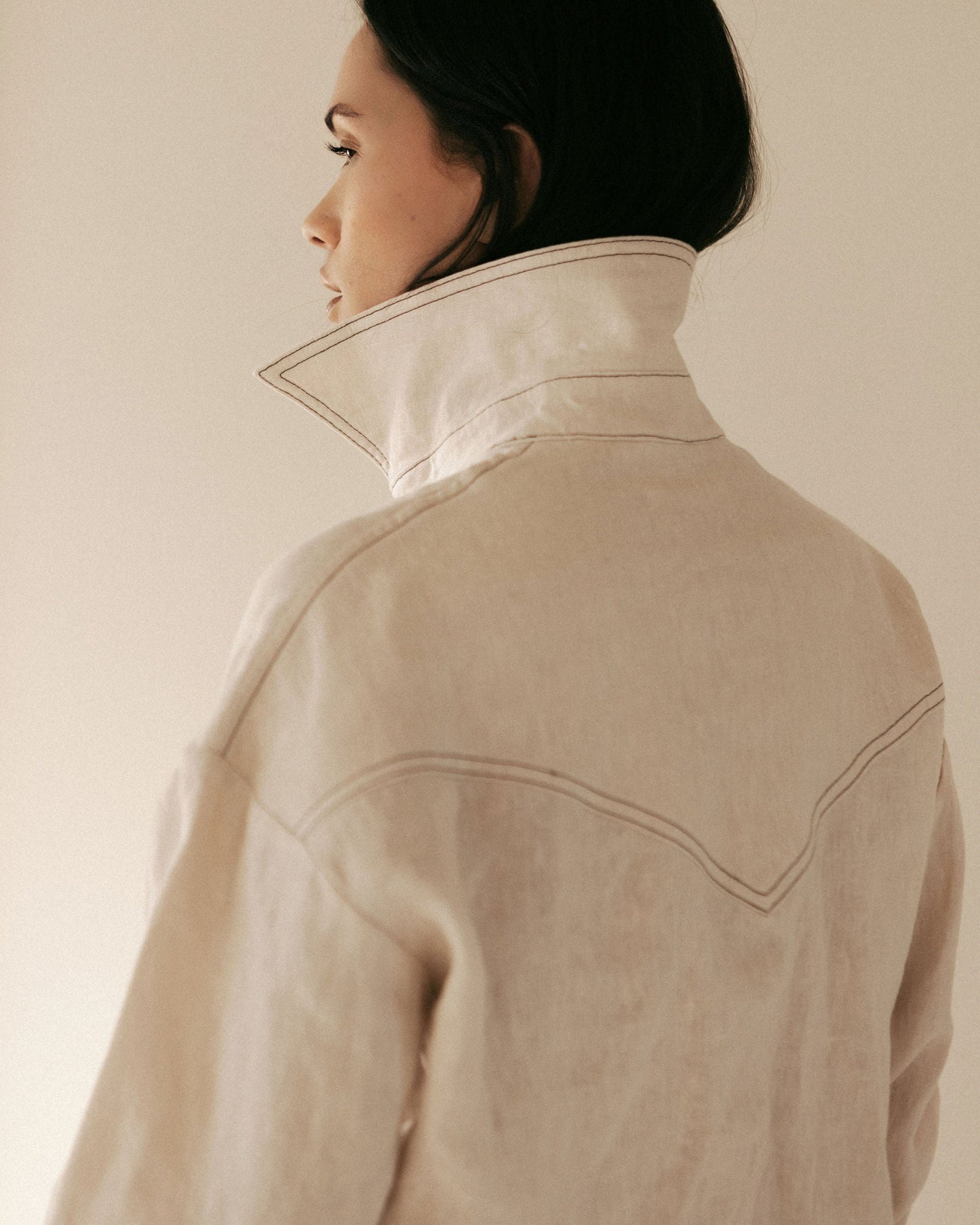 Person wearing a beige jacket against a plain background