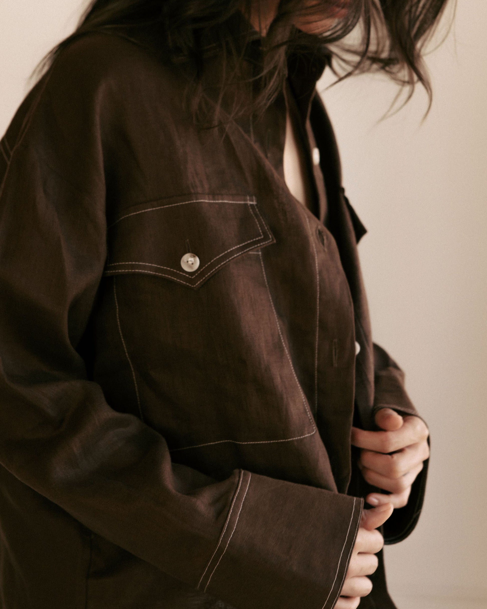 Close-up of a person wearing a dark brown jacket with a visible button on a plain background