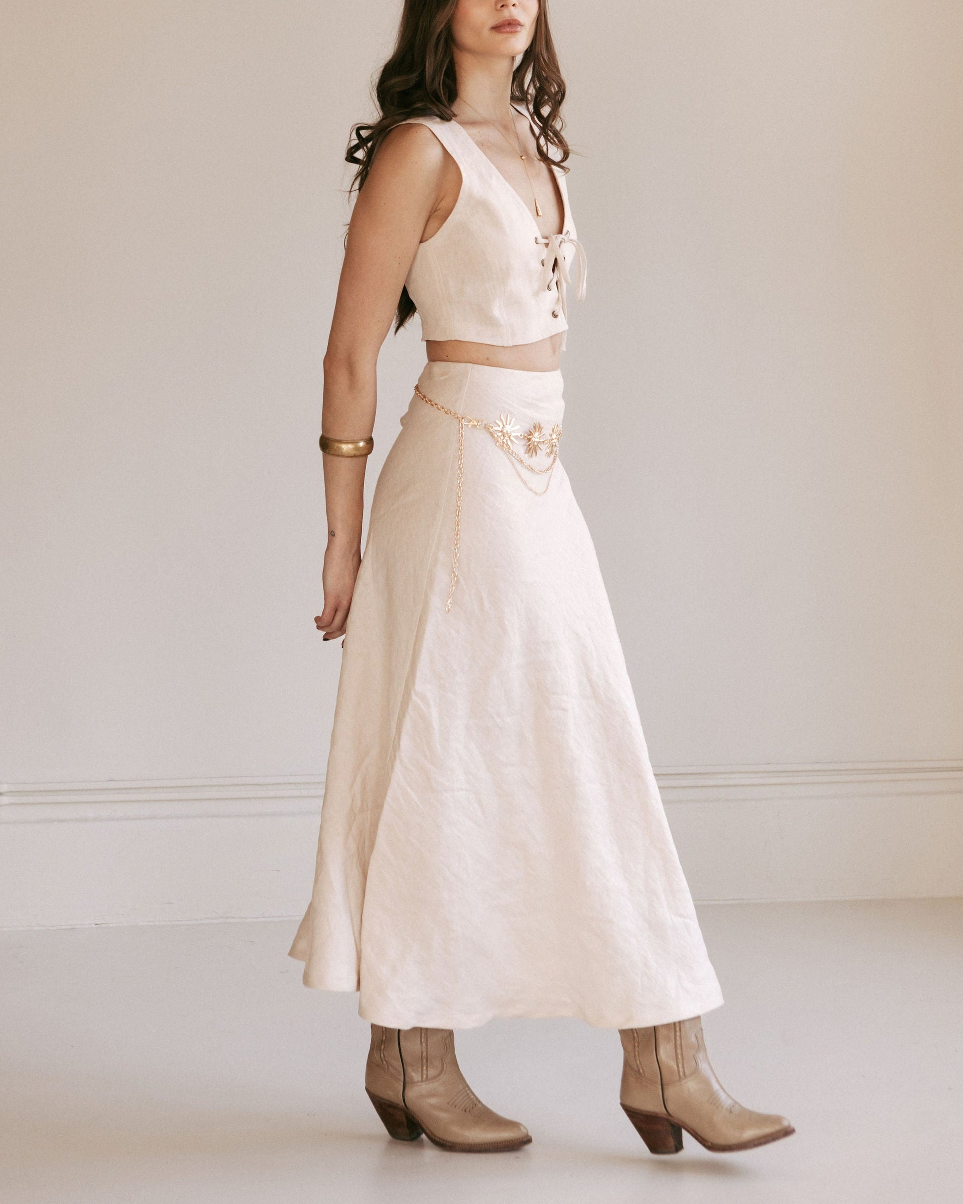 Woman wearing a white dress with a belt and boots against a plain background